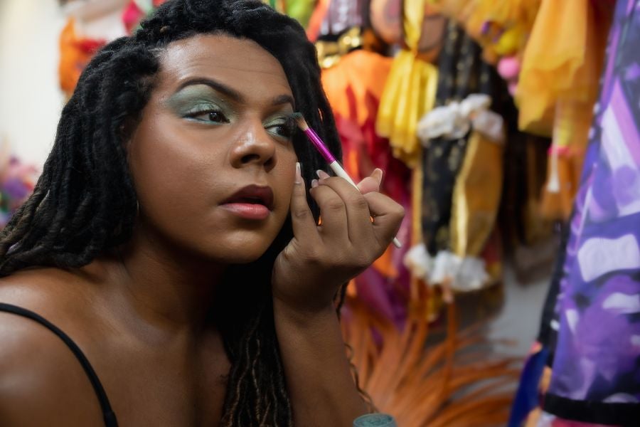 Mulher negra aplicando sombra colorida nos olhos para maquiagem para festival.