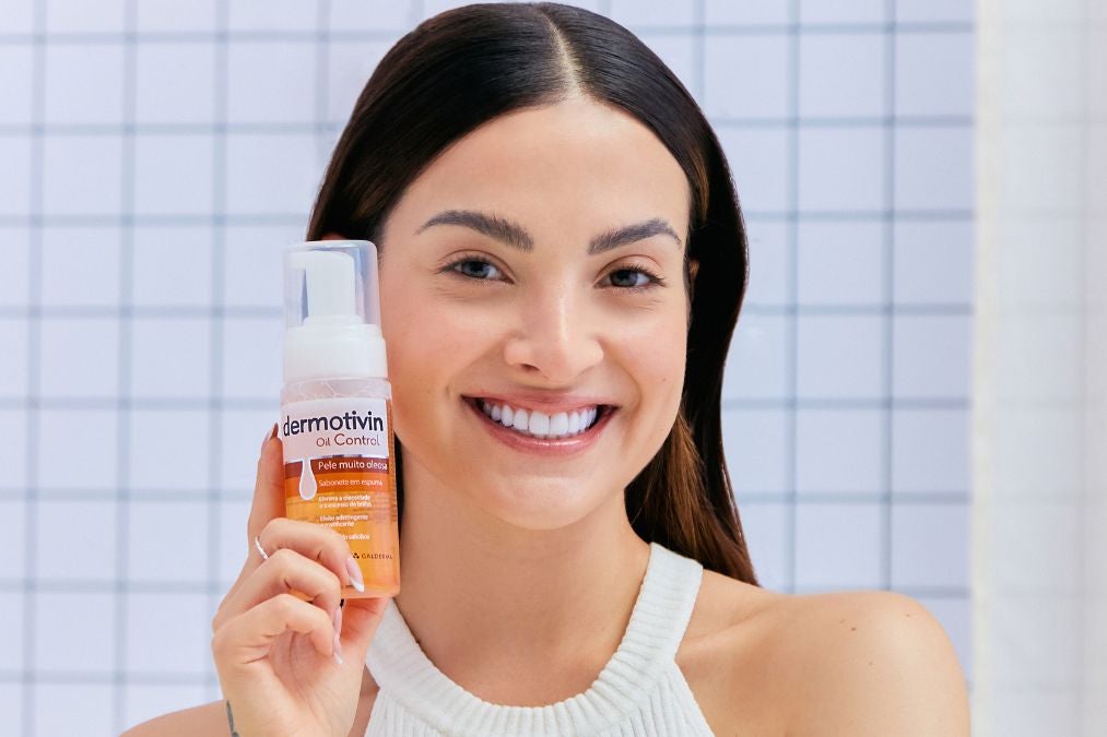 Mulher branca sorrindo e segurando sabonete em espuma Oil Control da Dermotivin para pele muito oleosa.