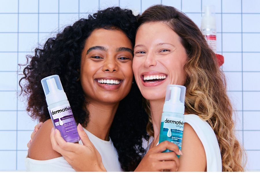 Duas mulheres juntas com diferentes tipos de pele sorrindo e segurando Dermotivin Soft e Dermotivin Original.